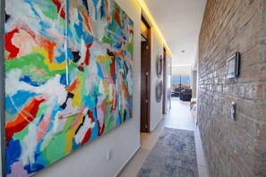Un couloir orné d’un tableau abstrait aux couleurs vives, avec un mur en pierre et une vue sur un espace de vie comprenant un canapé et une table.