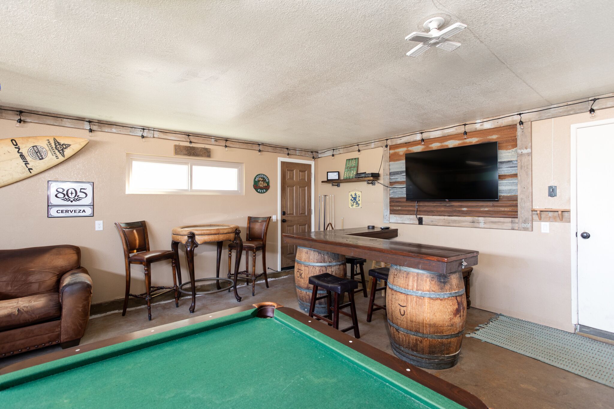 A pool table, bar area with stools, and a television mounted on the wall.