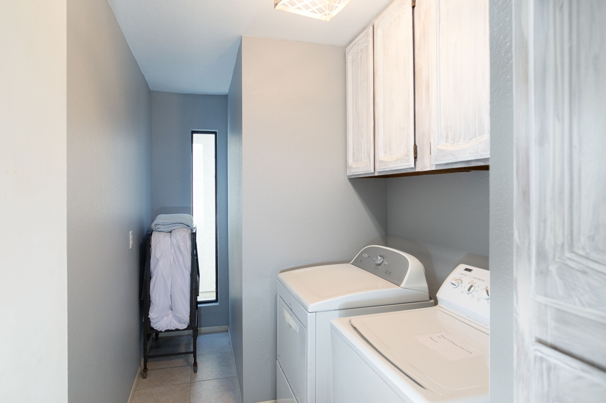 Un cuarto de lavandería con lavadora y secadora, un tendedero con ropa y una ventana que proporciona luz natural.