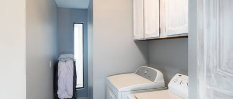 Un cuarto de lavandería con lavadora y secadora, un tendedero con ropa y una ventana que proporciona luz natural.