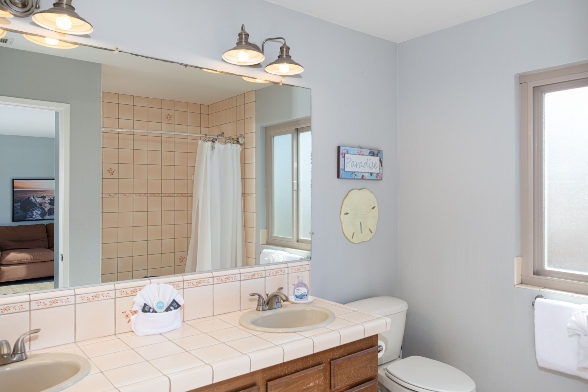 A bathroom with two sinks, a toilet, a large mirror, and a window.