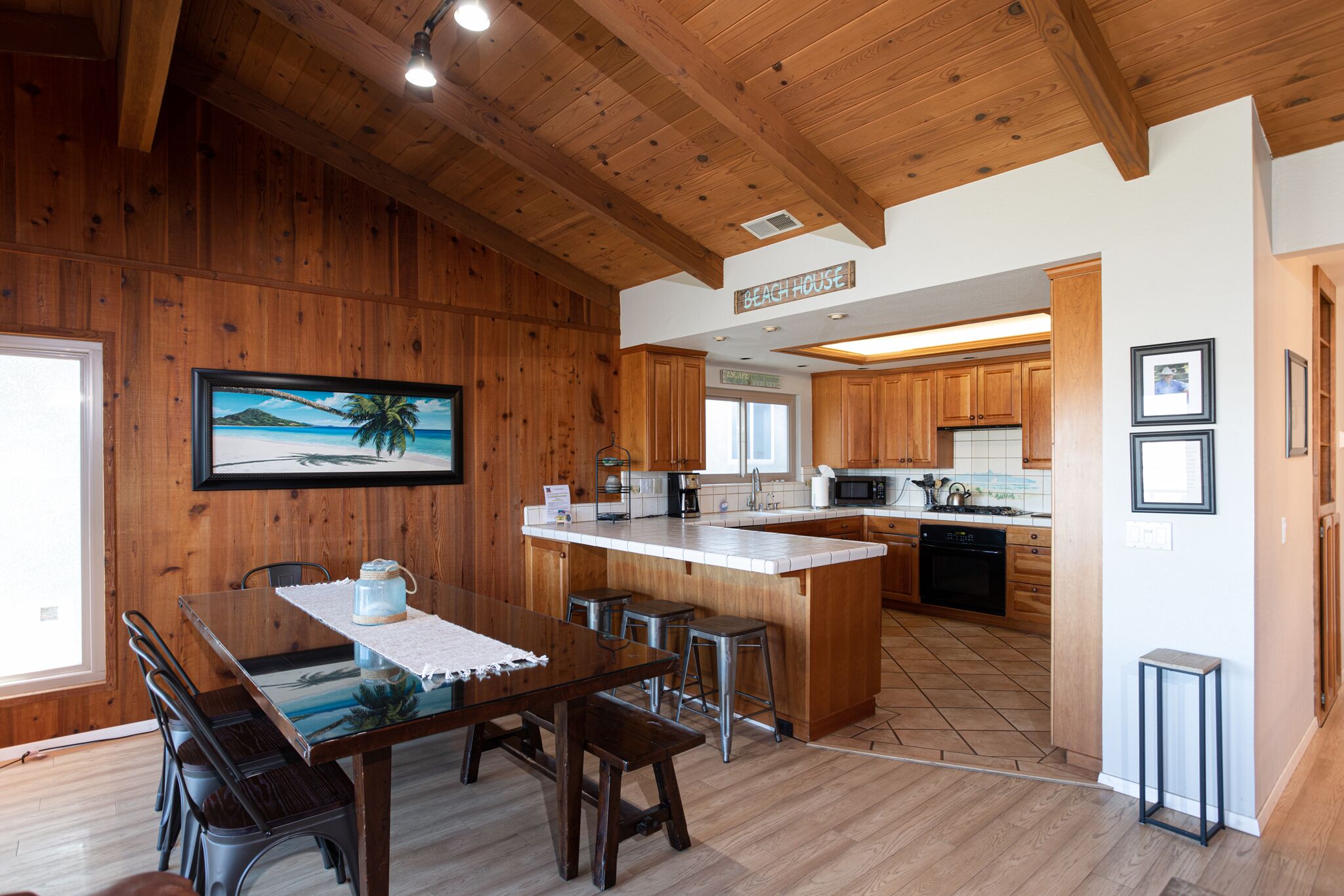 A wooden interior with a dining area, kitchen, and a sign reading "Beach House".