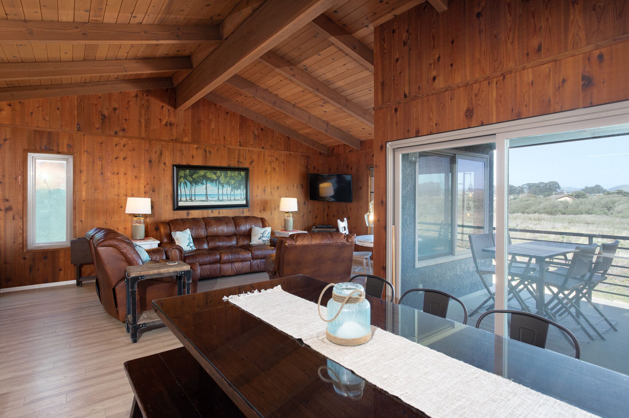 A wooden interior with a leather sofa, a glass dining table, and a TV mounted on the wall.
