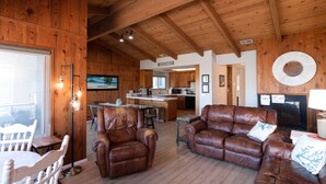 A spacious living area with leather sofas, a dining table, and a kitchen in the background.