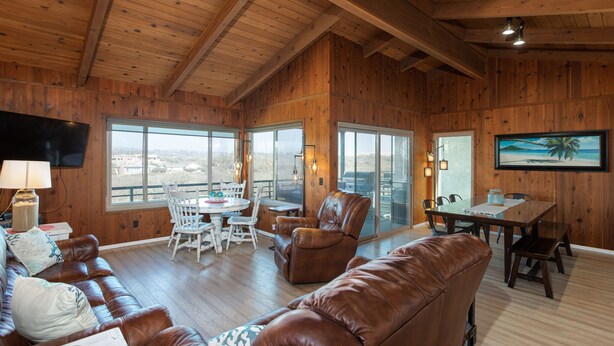 A spacious living area with wooden walls, a leather sofa, a dining table, and large windows offering a view.
