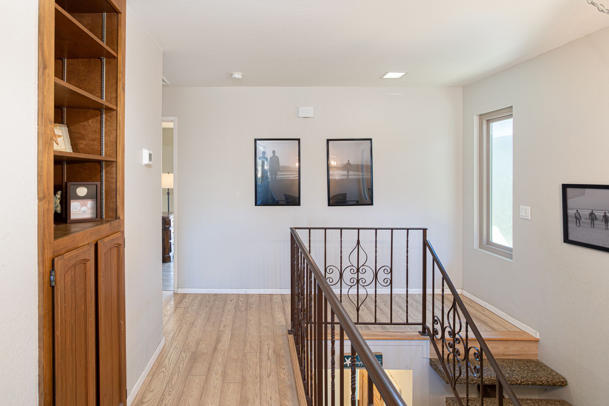 A staircase with a wooden finish and metal railings, leading to a landing with two framed pictures.