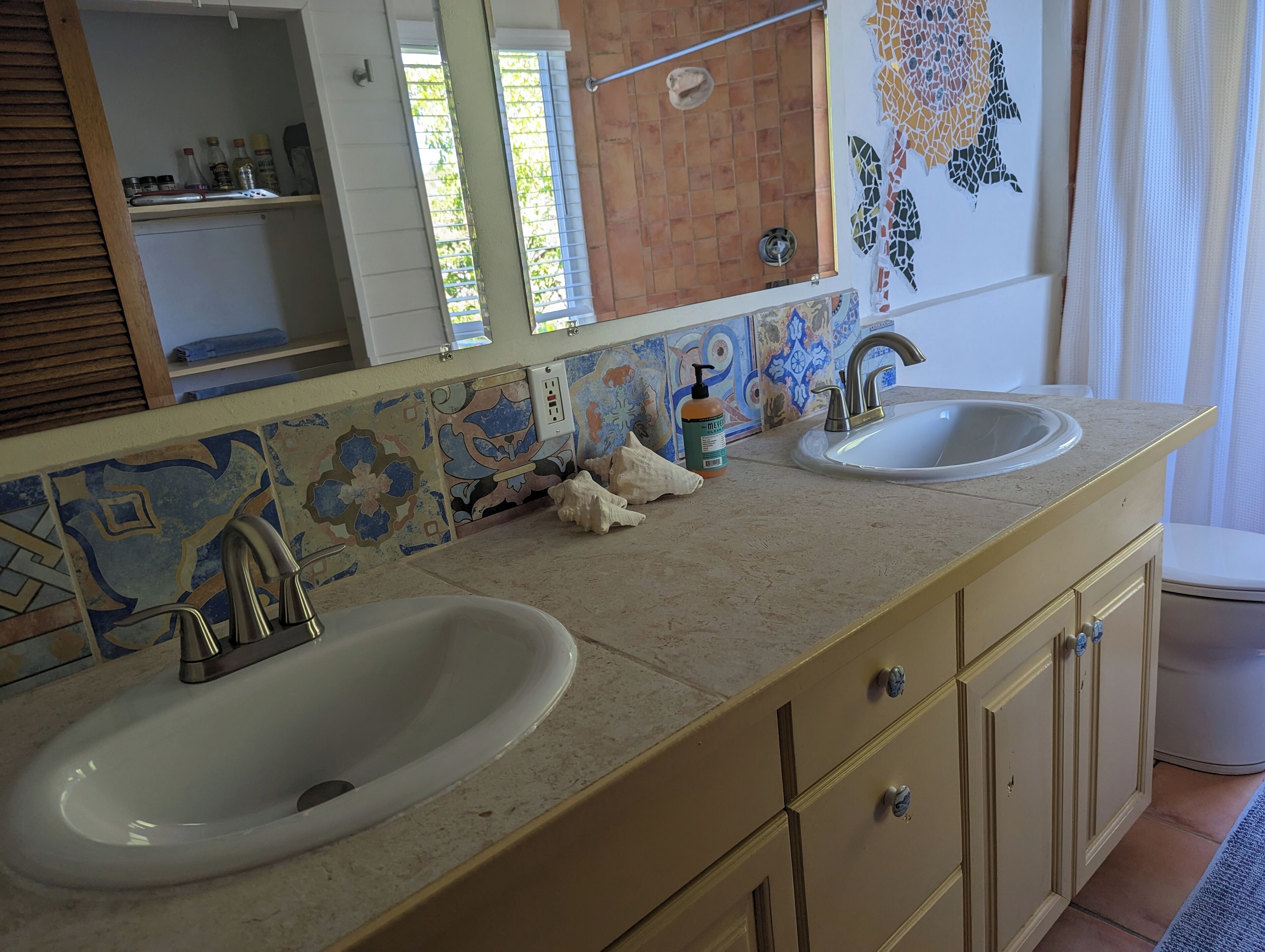 Une salle de bain avec deux lavabos, un miroir et un mur recouvert de carreaux.