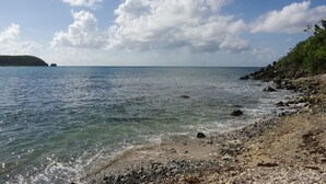 Une côte rocheuse bordée d’une eau claire, avec une île visible au loin.