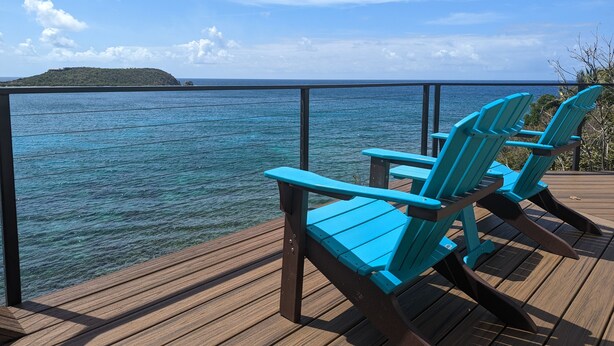 Une terrasse avec deux chaises Adirondack bleues, donnant sur une mer d’un bleu limpide et une île lointaine.