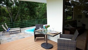 Un balcon agrémenté de meubles en osier, d’une table en verre et offrant une vue sur une piscine et un espace verdoyant.