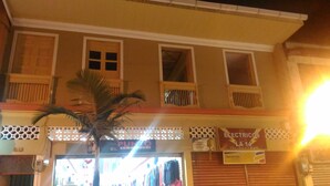 A building with multiple windows and balconies, a palm tree in front, and a storefront with a sign that reads "ELECTRICOS LA 14". - Hostal Don Jose - Hostel (Santa Rosa de Cabal)