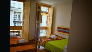A room with two beds, one with a green bedspread and the other with an orange bedspread. There is a chair and a small table in the room. - Hostal Don Jose - Hostel (Santa Rosa de Cabal)