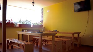 A room with wooden benches and tables, a TV mounted on the wall, and a window with potted plants. - Hostal Don Jose - Hostel (Santa Rosa de Cabal)