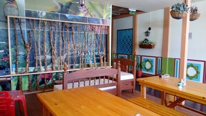 A restaurant interior with wooden furniture, a wall with a nature-themed mural, and hanging plants. - Hostal Don Jose - Hostel (Santa Rosa de Cabal)