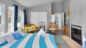 Ein Schlafzimmer mit Bett, Kommode, Sessel, Kamin und einem Fenster mit Vorhängen.