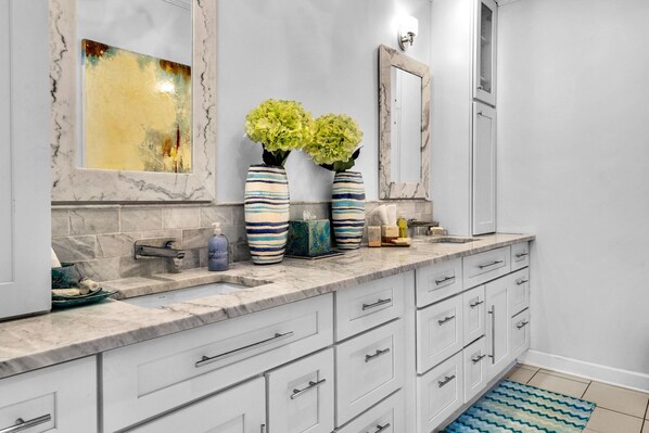 A modern bathroom with white cabinetry, a marble countertop, and a large mirror.