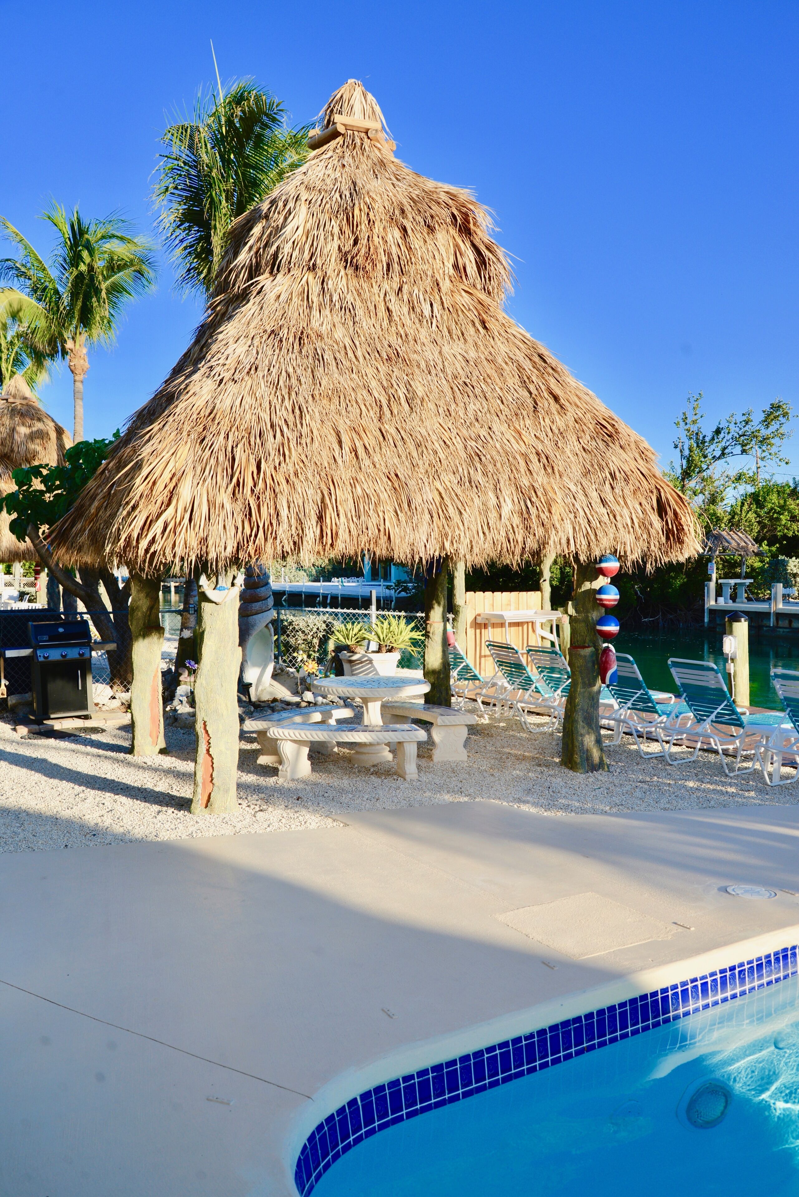 A poolside area with a thatched umbrella, lounge chairs, and a barbecue grill.
