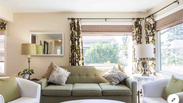 A living room with a sofa, two armchairs, a coffee table, a lamp, a mirror, and curtains.
