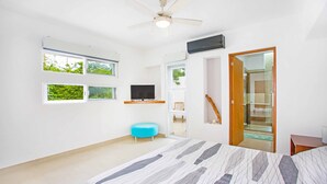 Een moderne slaapkamer met een groot bed, een plafondventilator, een flatscreen-tv en een raam met uitzicht op groen.