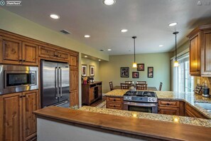 A kitchen with wooden cabinets, stainless steel appliances, granite countertops, and pendant lighting.