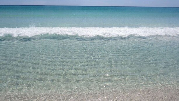 Una playa con aguas claras y poco profundas, y una orilla arenosa visible.