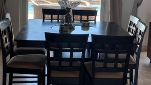 Un comedor con una mesa y sillas, vista al océano y palmeras a través de un ventanal, y una señal de salida sobre la puerta.