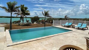 Una piscina con sillas de descanso, palmeras y vistas al océano.
