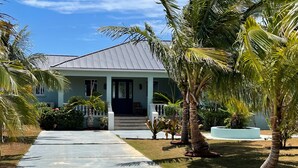 Una casa con porche cubierto, palmeras y un césped cuidado.