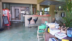 Un espace bar avec un comptoir, deux tabourets de bar noirs, une chaise verte et une table sur laquelle se trouvent des livres et un grand récipient.