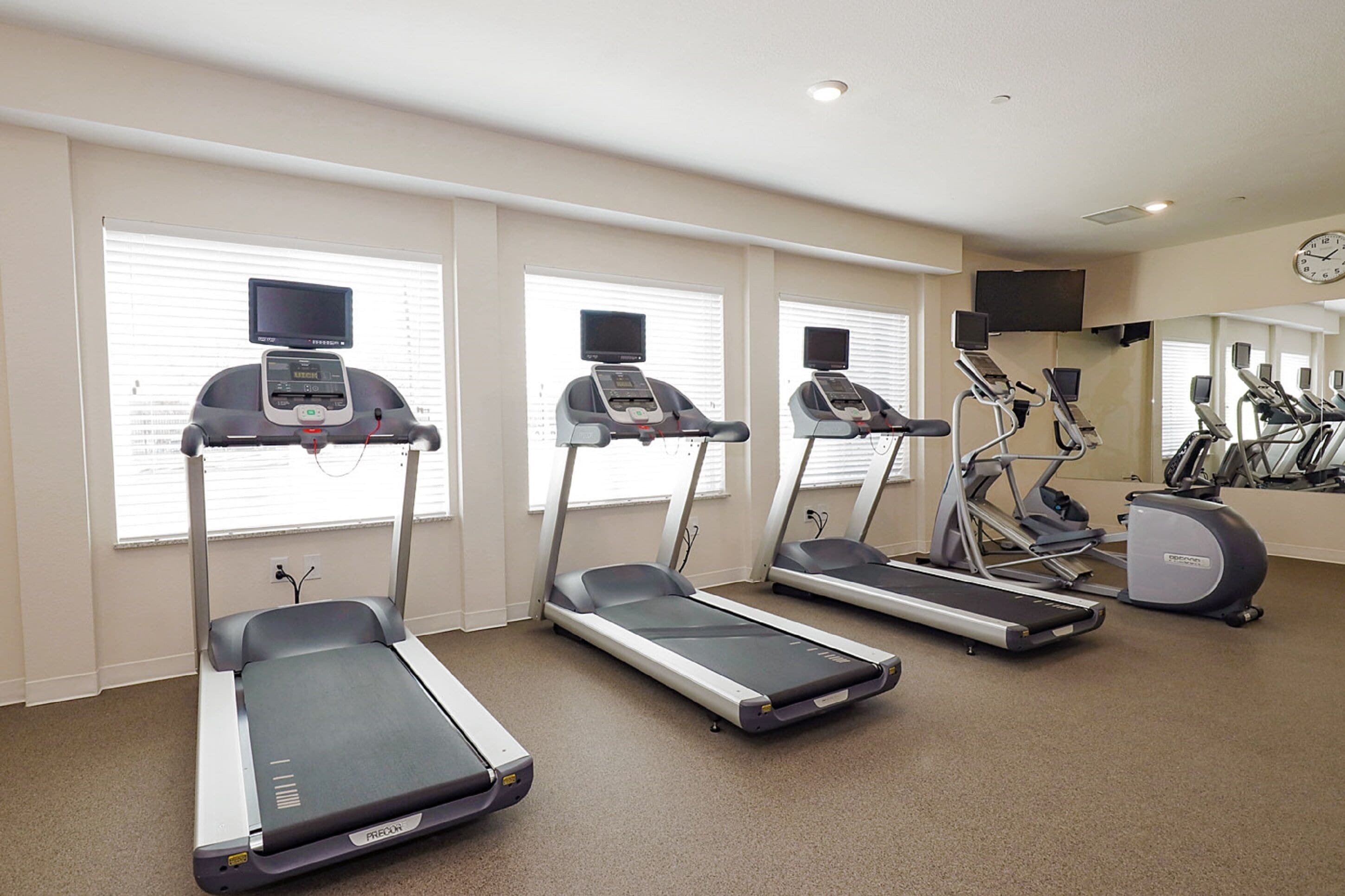 A fitness room with treadmills, elliptical machines, and a TV screen on each machine.