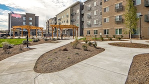 A multi-story building with a brick facade, a flag, and a covered outdoor seating area with benches. - Parks Residential -Richardson (Richardson)