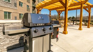 An outdoor grill area with a stone wall and a wooden pergola. - Parks Residential -Richardson (Richardson)
