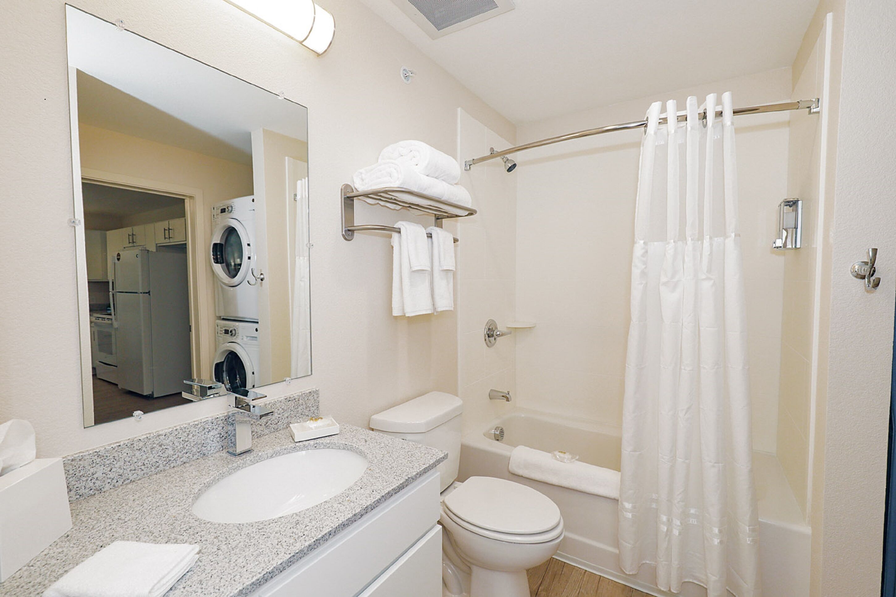 A modern bathroom with a granite countertop sink, a toilet, a bathtub, and a shower curtain.