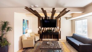 A modern living room with a TV mounted on a wooden wall, a sofa, a coffee table, and a potted plant. - Parks Residential -Richardson (Richardson)