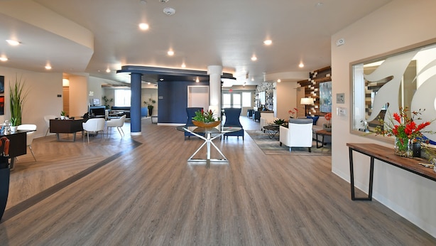 A spacious lobby with a modern design, featuring a central glass table, comfortable seating, and a large mirror on the right. - Parks Residential -Richardson (Richardson)