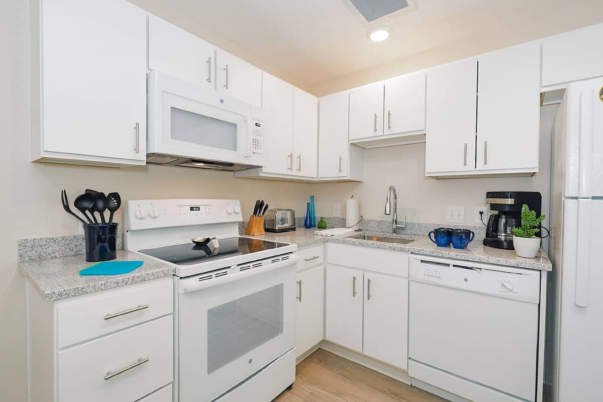 A modern kitchen with white cabinets, a microwave, stove, dishwasher, and various kitchen appliances.