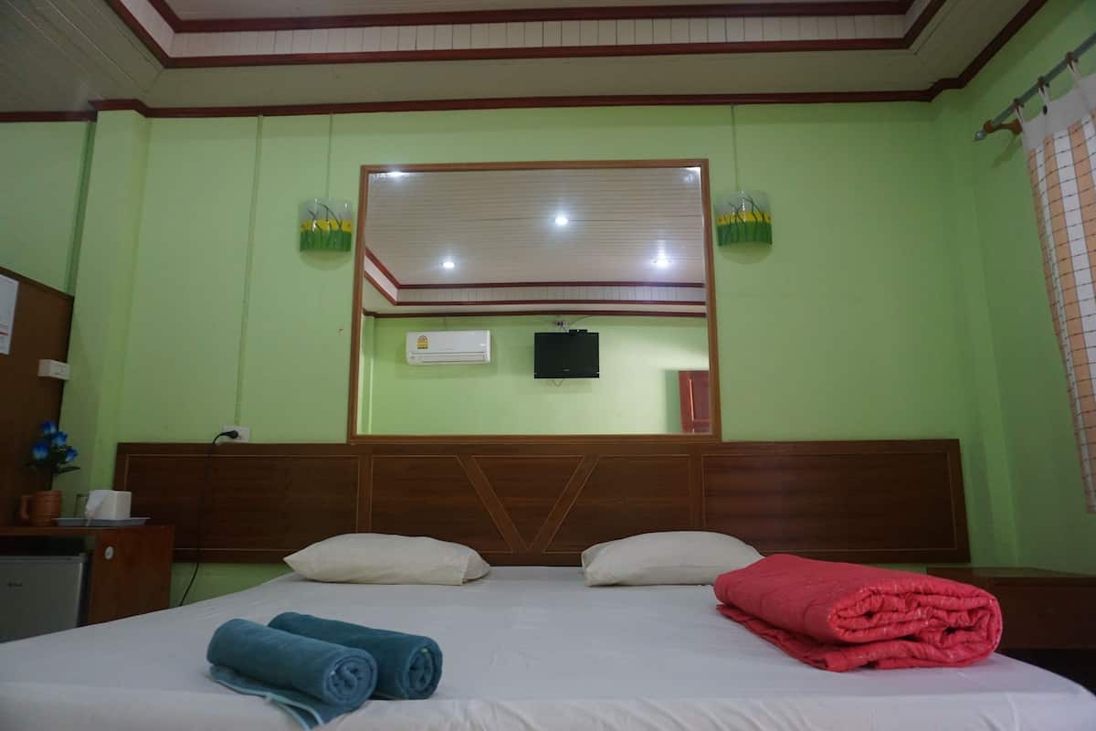 A hotel room with a bed, a wooden headboard, a flat-screen TV mounted above the bed, and a window with a curtain.