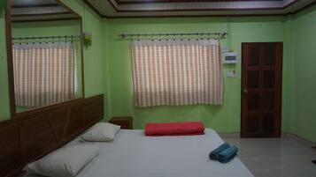 Quarto com uma cama de solteiro, cabeceira de madeira, toalha vermelha e janela com cortina xadrez.