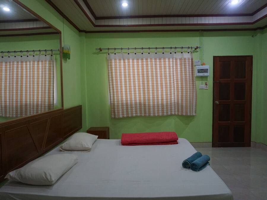 Quarto com uma cama de solteiro, cabeceira de madeira, toalha vermelha e janela com cortina xadrez.