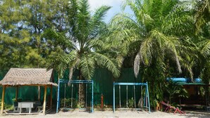 A covered outdoor area with a table and chairs, a swing set, and a fenced area with palm trees.