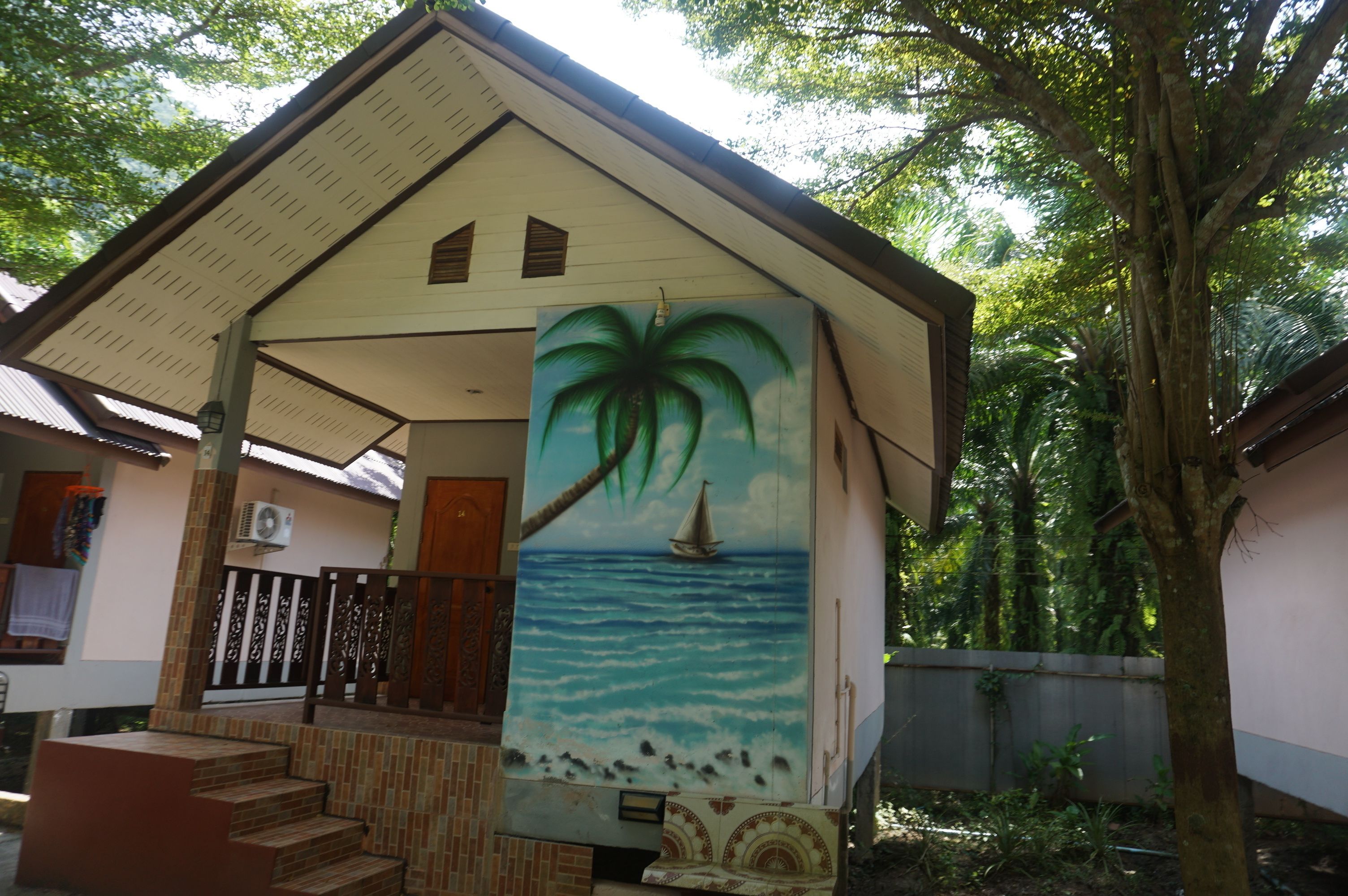 Una casa con fachada de tejas, una escalera que conduce a un porche, y un mural con una palmera y un velero en la pared.
