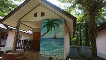 Una casa con fachada de tejas, una escalera que conduce a un porche, y un mural con una palmera y un velero en la pared.