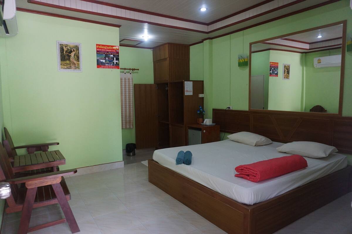 A room with a bed, a wooden chair, a wardrobe, and a mirror.