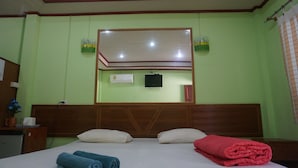 A hotel room with a bed, a wooden headboard, a flat-screen TV, and a window with a curtain.