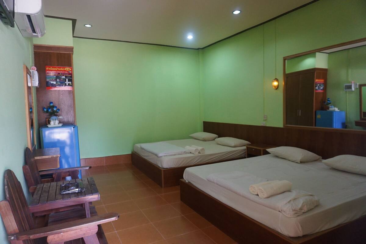 A hotel room with two single beds, a wooden desk, a small table, and a refrigerator.