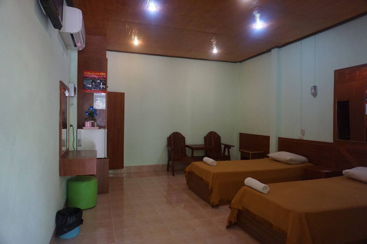 A hotel room with two beds, a desk, a chair, a small table, a mirror, a trash bin, and a wall-mounted air conditioner.