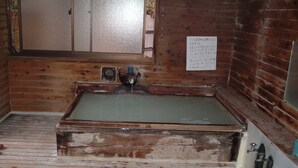 Une petite pièce rustique en bois, avec une baignoire, une petite fenêtre et un banc en bois.