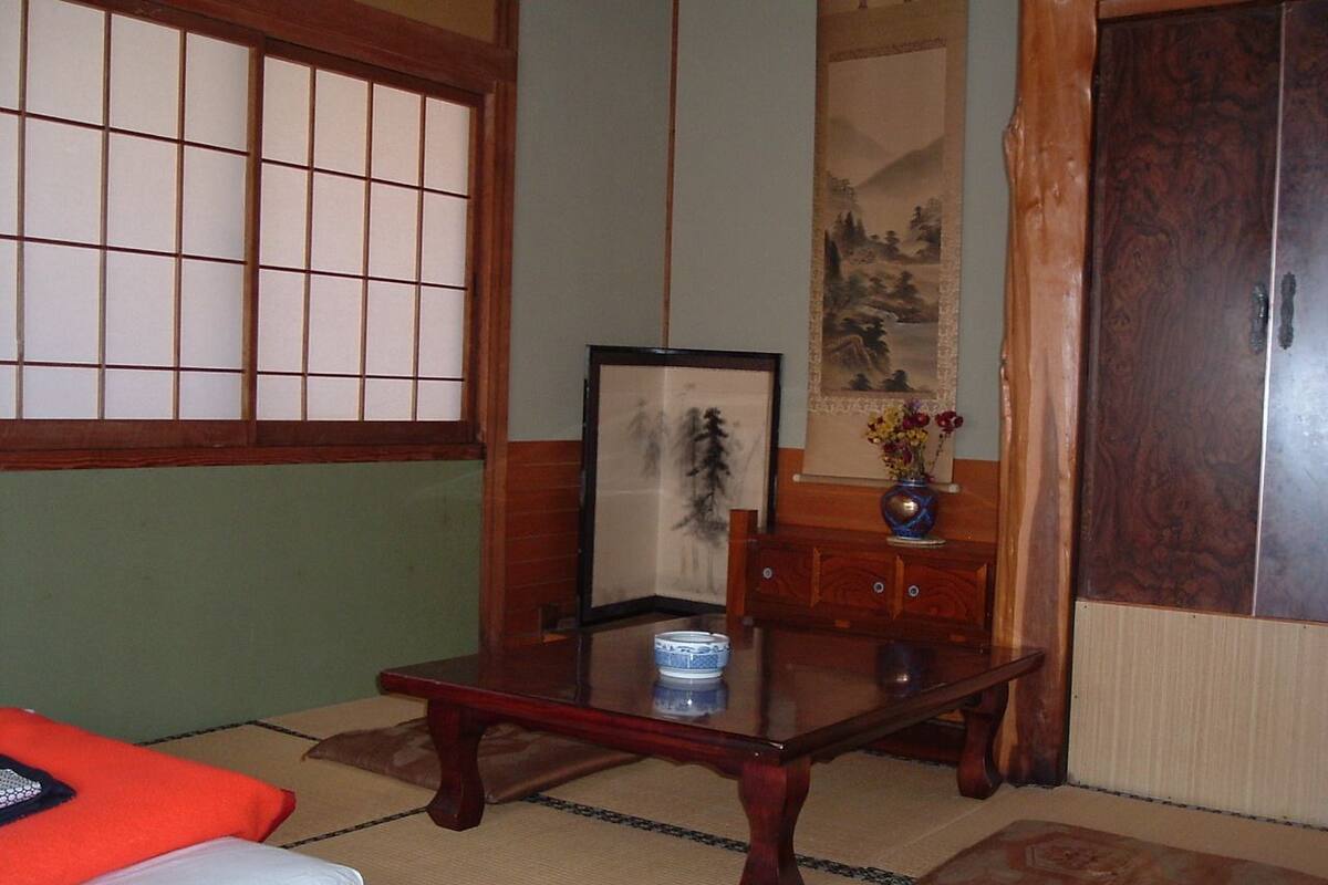 A traditional Japanese room with tatami flooring, a low wooden table, a futon bed, a shoji screen, and a calligraphy scroll.