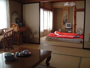 A traditional Japanese room with tatami flooring, a low table with tea set, a bed with red bedding, and a television on a stand. - Onsen Inn 36So (Matsumoto)