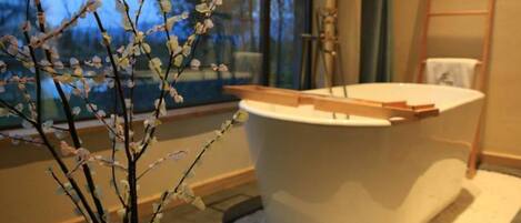 A modern bathroom with a freestanding bathtub, a window with a view of trees, and a ladder against the wall.